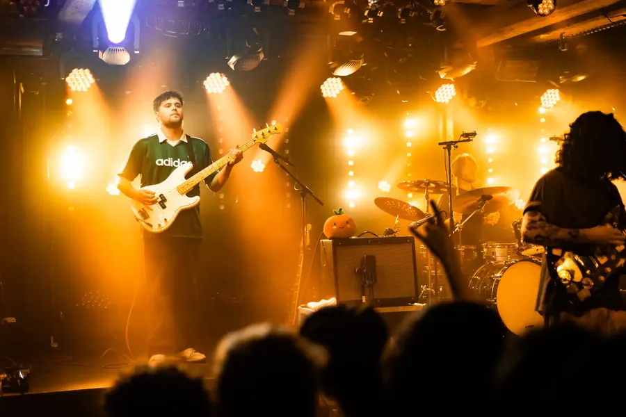 Band auf der Bühne in orangem Licht, Gitarrist im grünen Shirt – Fomies live im Salzhaus Winterthur, 2025
