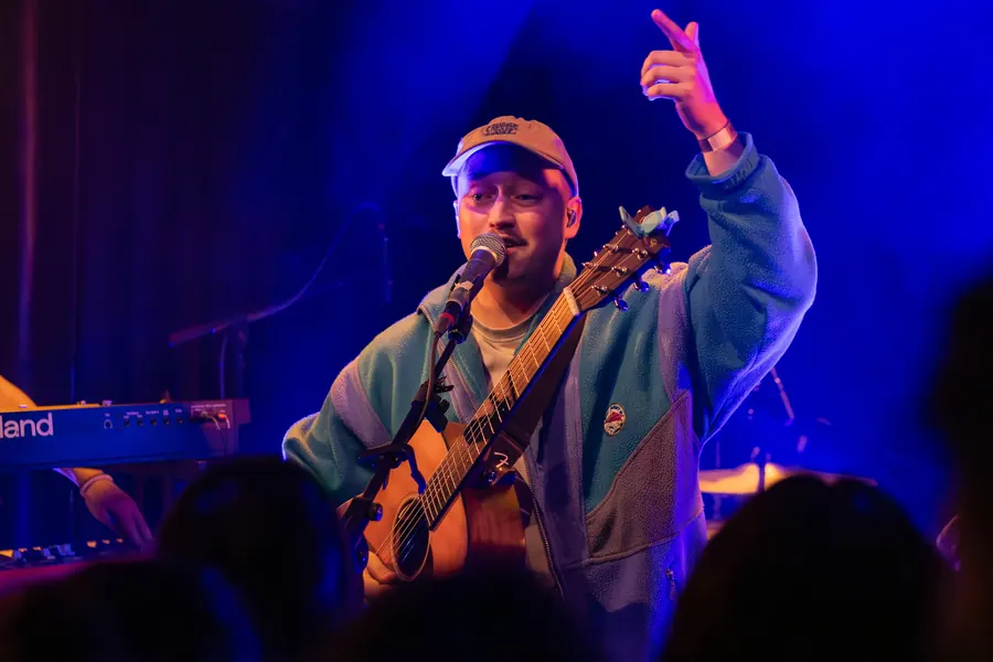 Sänger mit Gitarre und Cap streckt die Hand in die Luft – Lhanzom Lhasam & Noah Parks live im Albani Winterthur, 2025