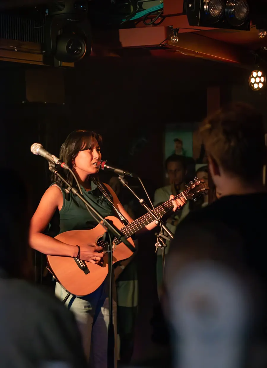 Sängerin mit Akustikgitarre am Mikrofon – Lhanzom Lhasam & Noah Parks live im Albani Winterthur, 2025