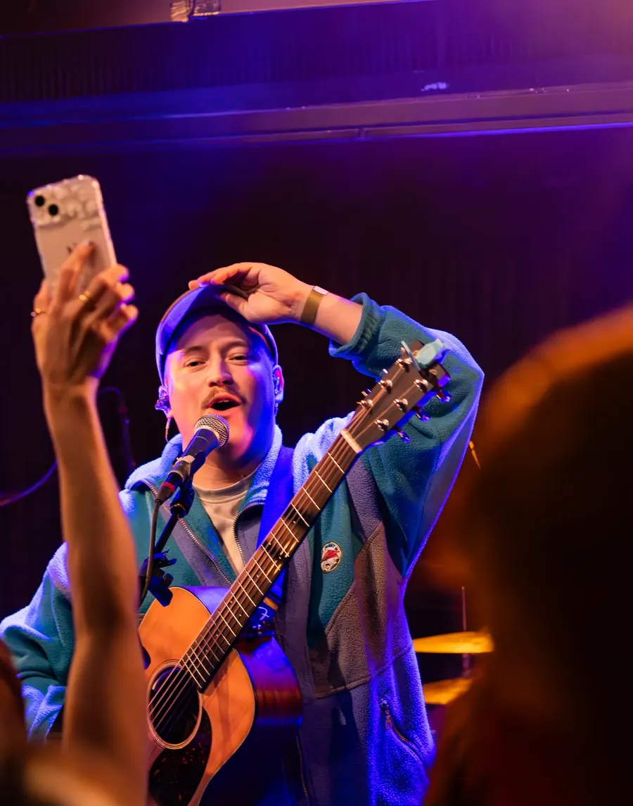 Sänger mit Gitarre macht ein Handyfoto vom Publikum – Lhanzom Lhasam & Noah Parks live im Albani Winterthur, 2025