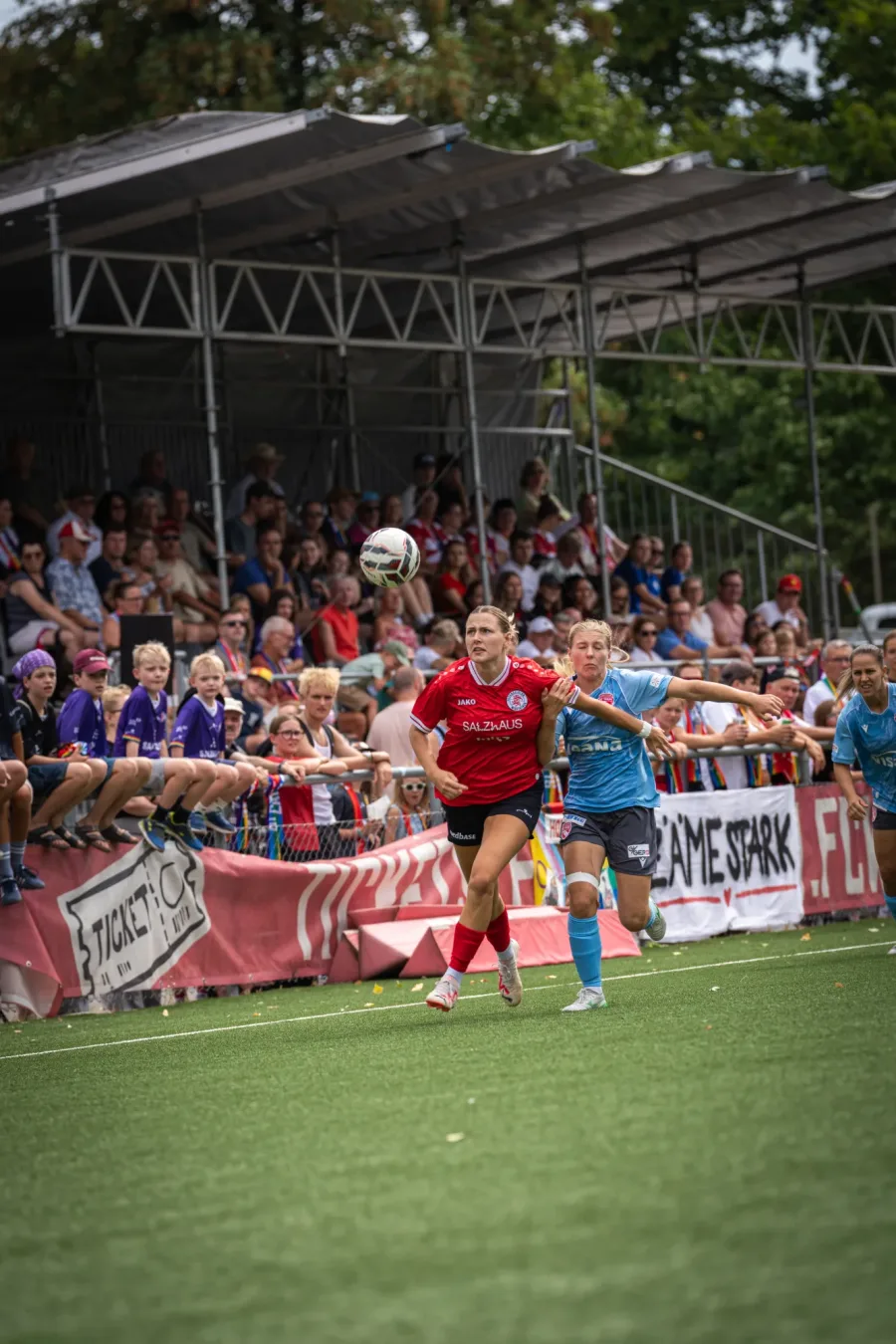 FCW-Spielerin in Rot im Zweikampf mit einer Thun-Spielerin in Hellblau vor vollen Rängen – FC Winterthur Frauen gegen FC Thun, 16. August 2026