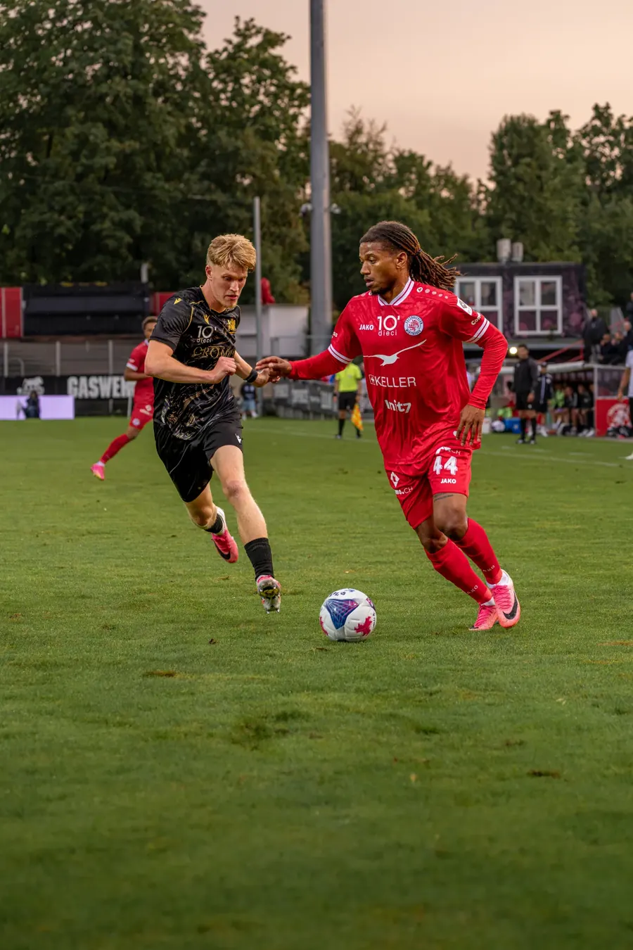 FCW-Spieler am Ball, ein Gegenspieler in Schwarz verfolgt ihn im Abendlicht – FC Winterthur gegen FC Stade Lausanne-Ouchy auf der Schützenwiese, 29. August 2026
