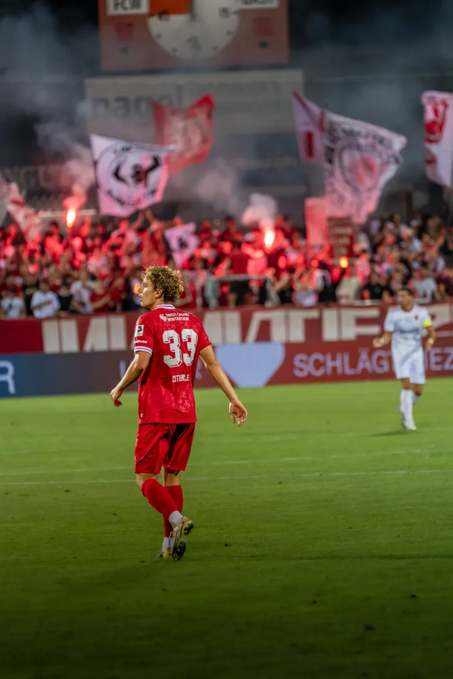 FCW-Spieler Nummer 33 vor der Fankurve mit Pyros und Fahnen – FC Winterthur, Heimspiel auf der Schützenwiese